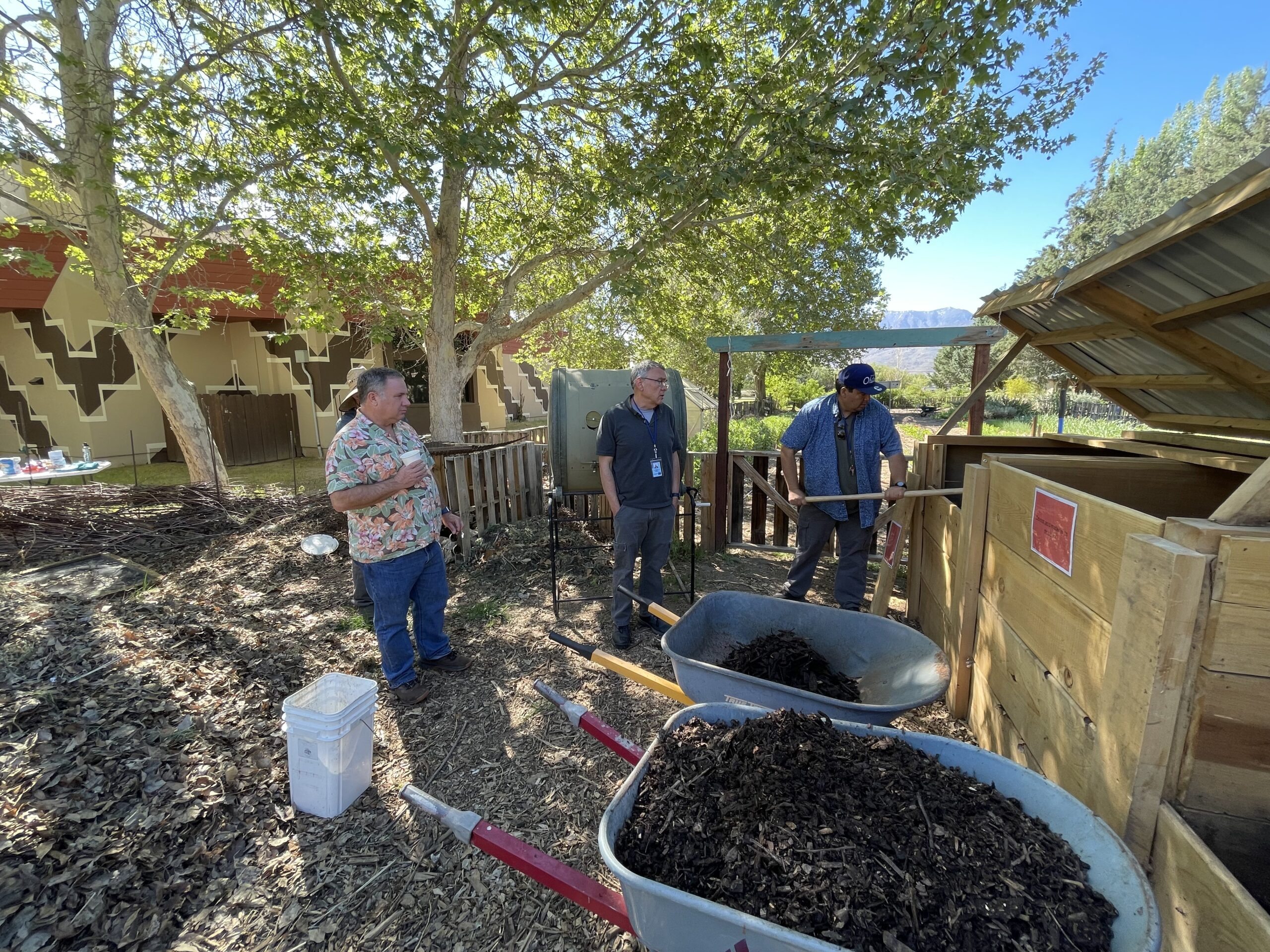 Three people standing next to compost bins, with two wheelbarrows full of compost.
