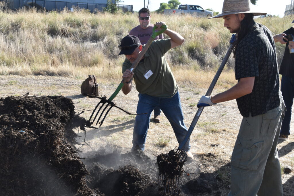 Three people turning a compost pile in a field